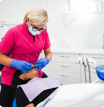 photo-team-3 Dental hygienist in pink uniform and mask treating a female patient reclined in a dental chair